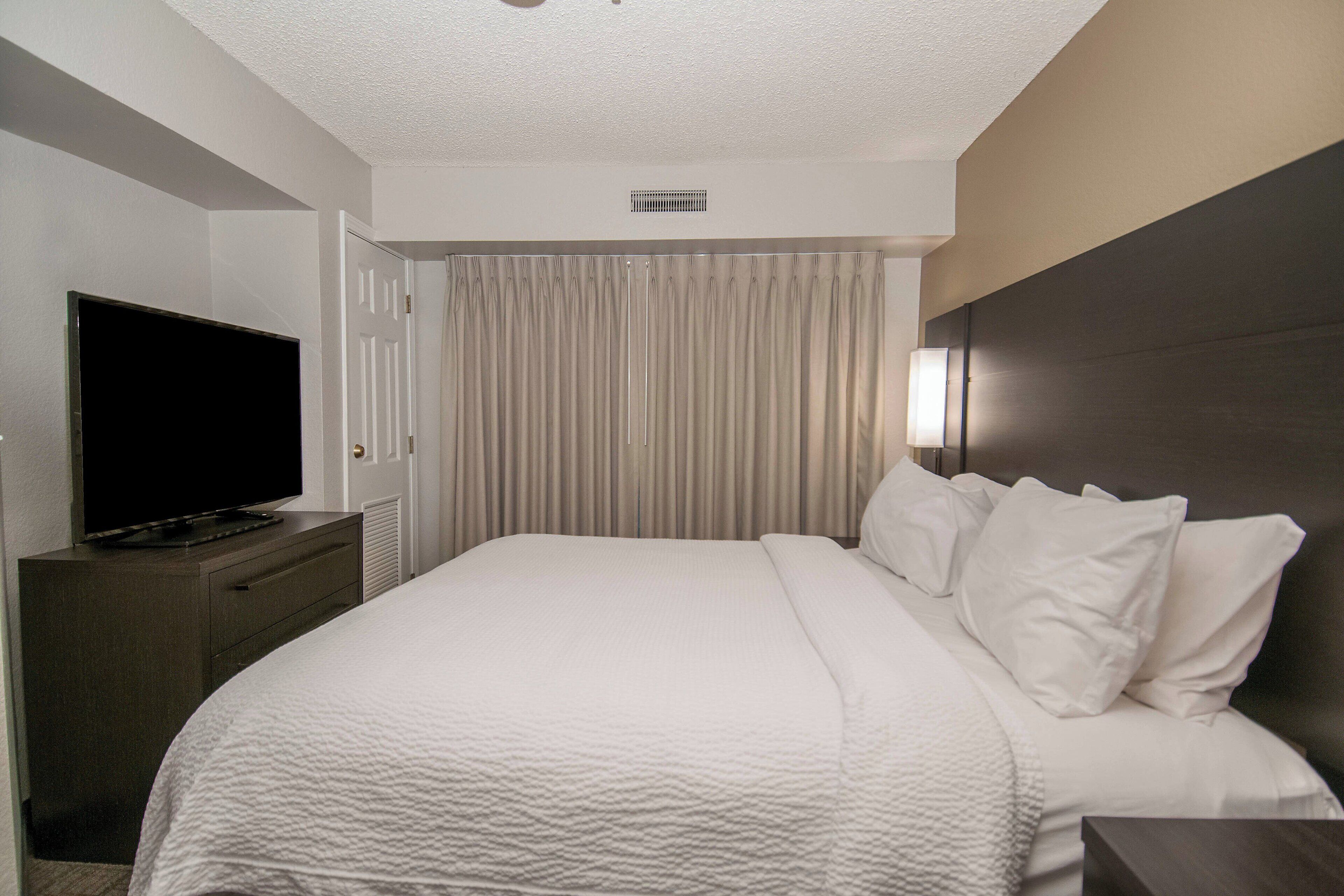 A hotel room with a large bed, a flat-screen TV on a dresser, a door, and a window with curtains.