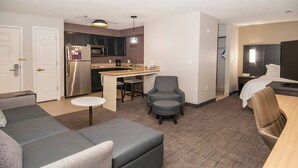 Ein kompaktes Hotelzimmer mit Küchenzeile, einer Couch, einem Essbereich und einem Bett.