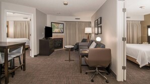 Ein Hotelzimmer mit Bett, Schreibtisch mit Stuhl, Sofa, Fernseher, Lampe und kleinem Tisch.