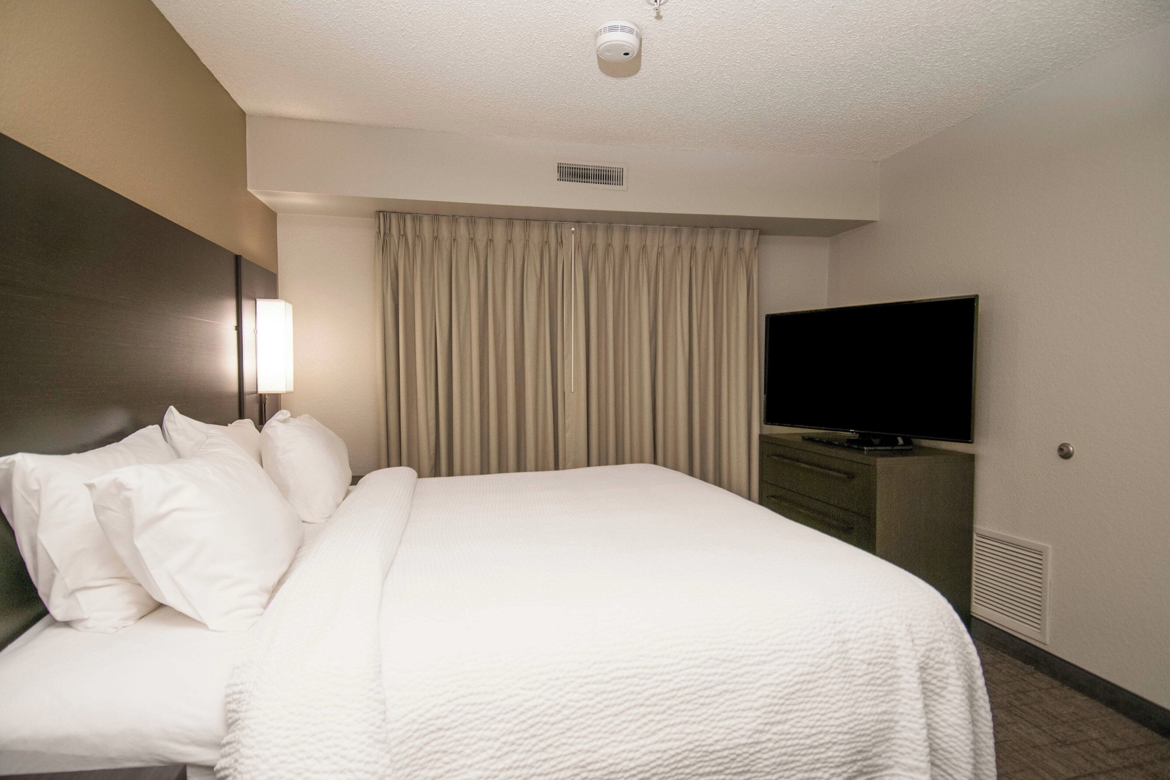 Habitación de hotel con cama, televisor, escritorio y ventana con cortinas.