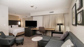 Ein Hotelzimmer mit Bett, einer Couch, einem Schreibtisch, einem Stuhl und einem Fernseher.
