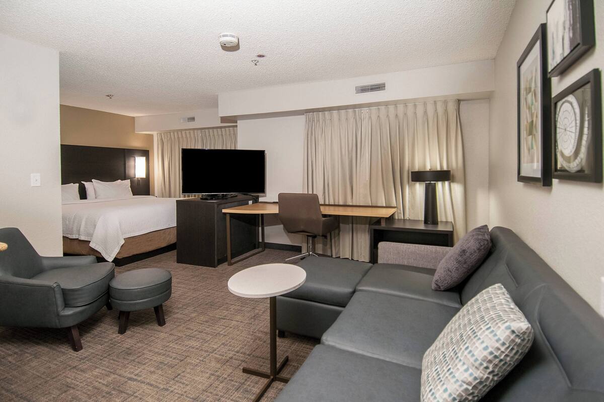 A hotel room with a bed, a sofa, a desk, a chair, and a television.