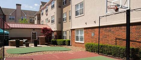 A basketball court adjacent to a building with a basketball hoop.