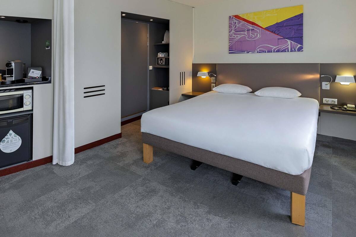 A hotel room with a bed, a desk with a computer, a microwave, and a small refrigerator.