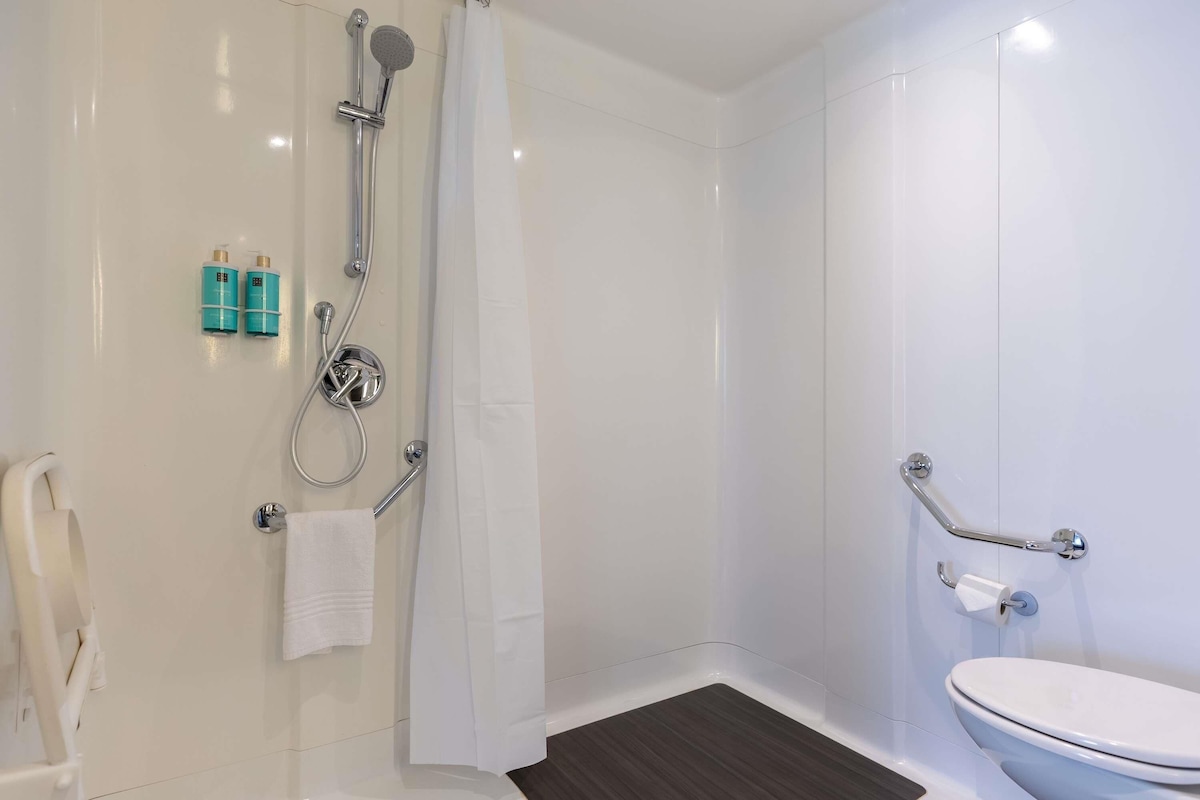 Un baño con ducha, inodoro y barras de apoyo.