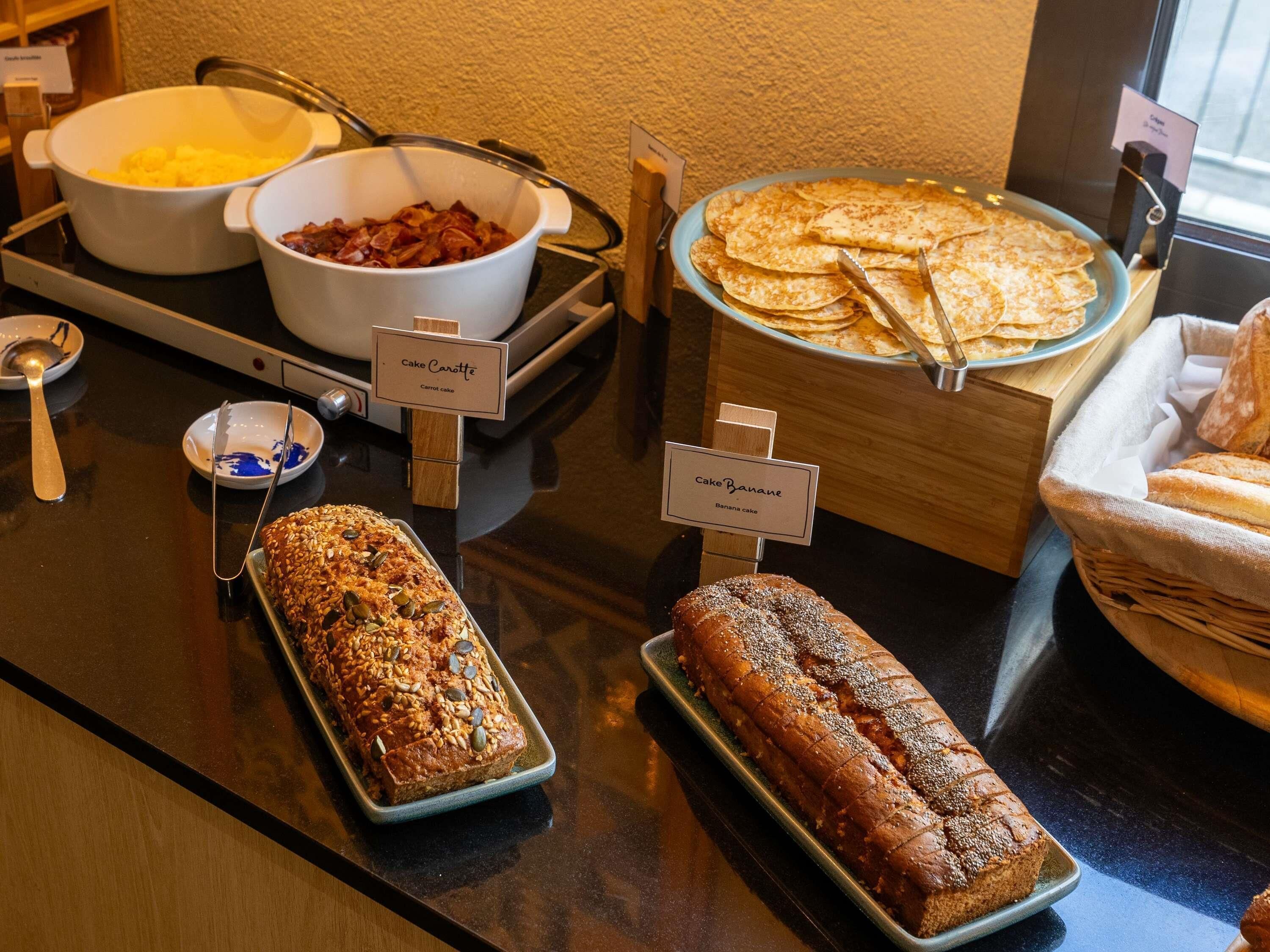 A buffet with labeled dishes including cake carrotte, cake banana, and a loaf of bread.