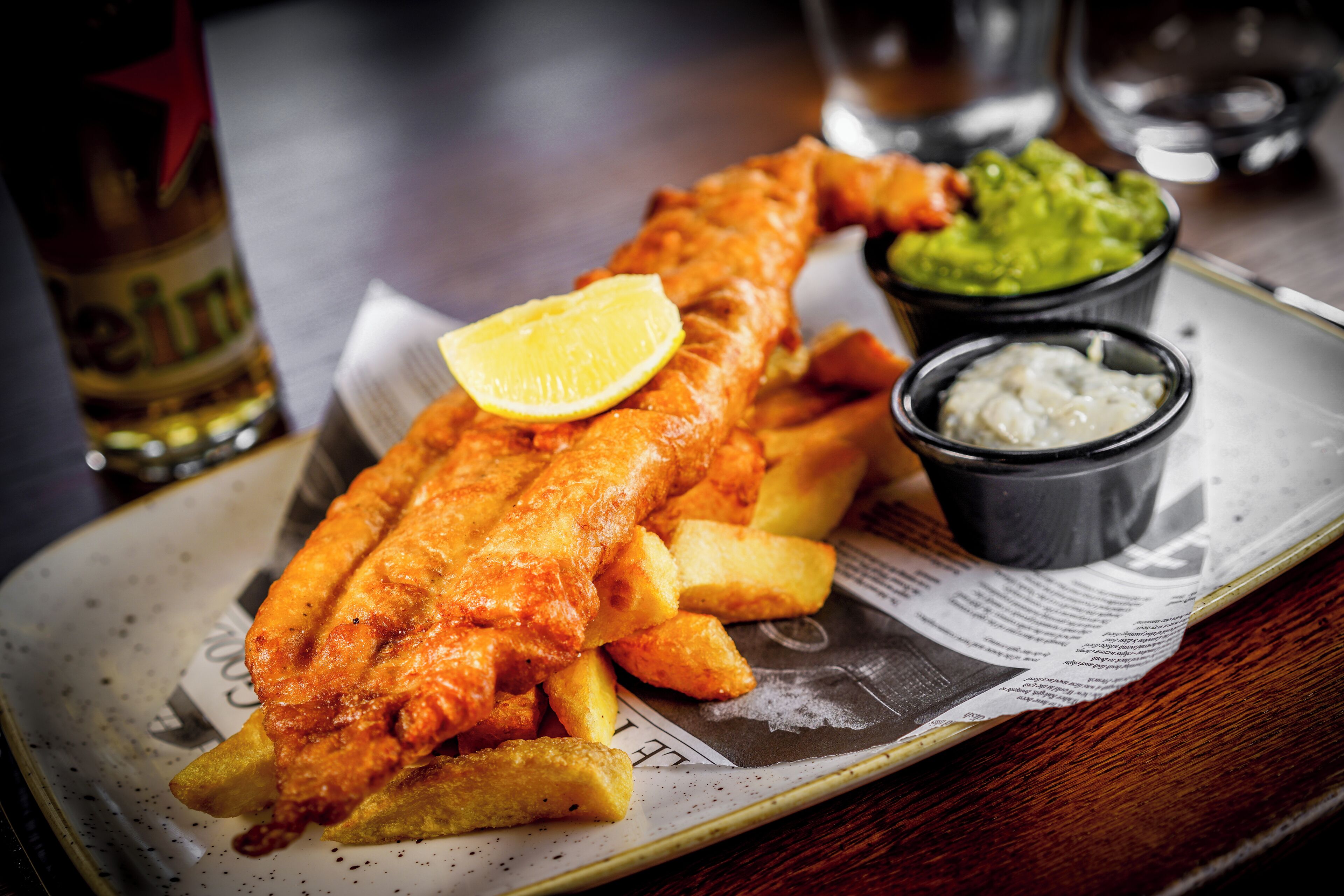Um prato de peixe com batatas fritas, fatias de limão e dois molhos.
