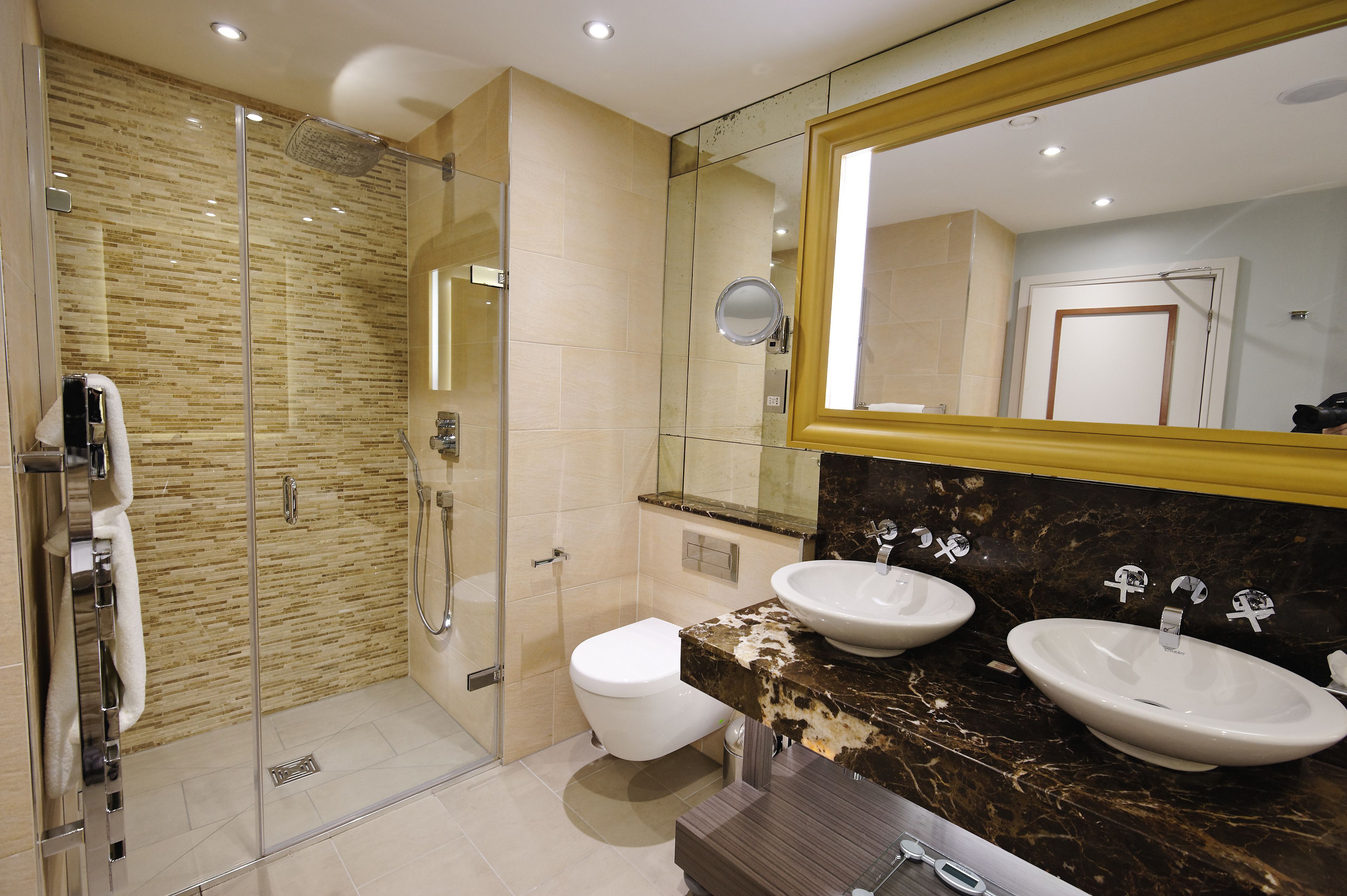 A modern bathroom with a glass-enclosed shower, a toilet, and two sinks with marble countertops.