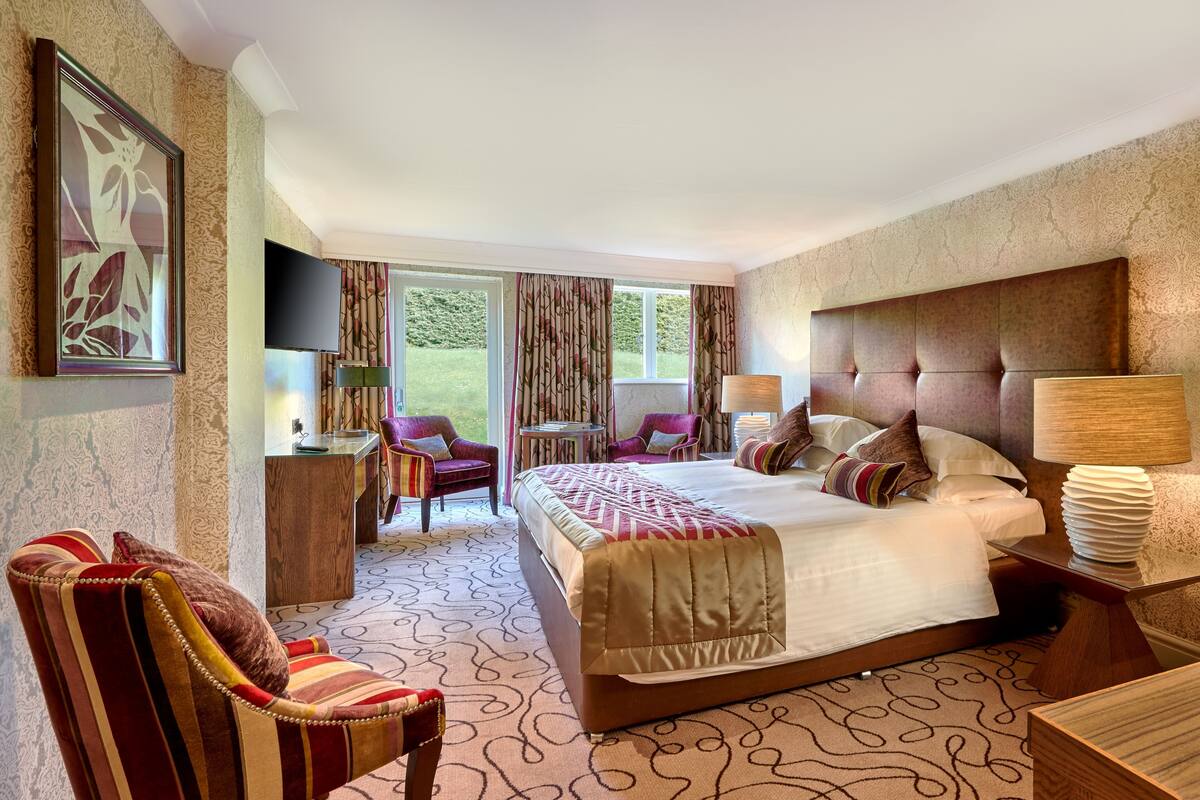 A hotel room with a large bed, a TV, a desk, and a chair.