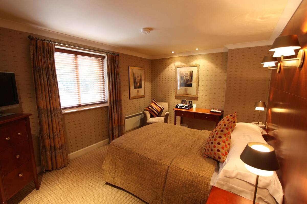 A hotel room with a bed, a desk, a chair, a television, and a window with curtains.