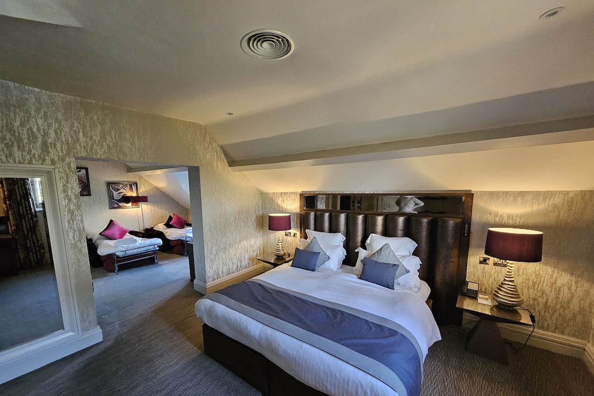 A spacious bedroom with a large bed, two bedside tables with lamps, and a view of another room.