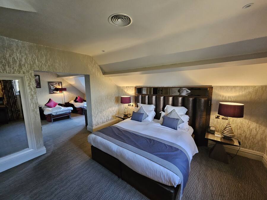 A spacious bedroom with a large bed, two bedside tables with lamps, and a view of another room.