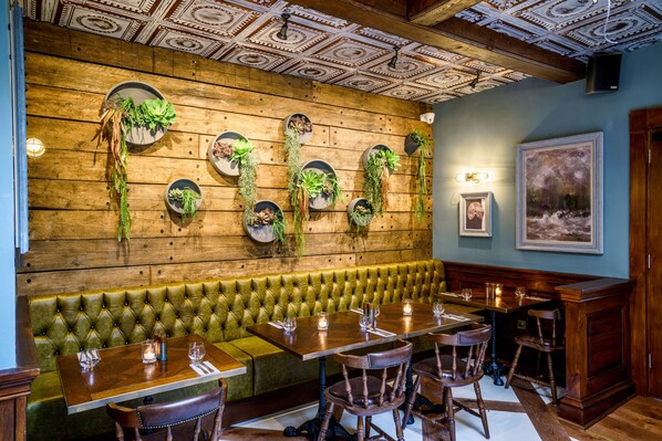 A restaurant with a wooden wall, green cushioned bench, wooden tables, and chairs. - Grosvenor Pulford Hotel & Spa (Chester)