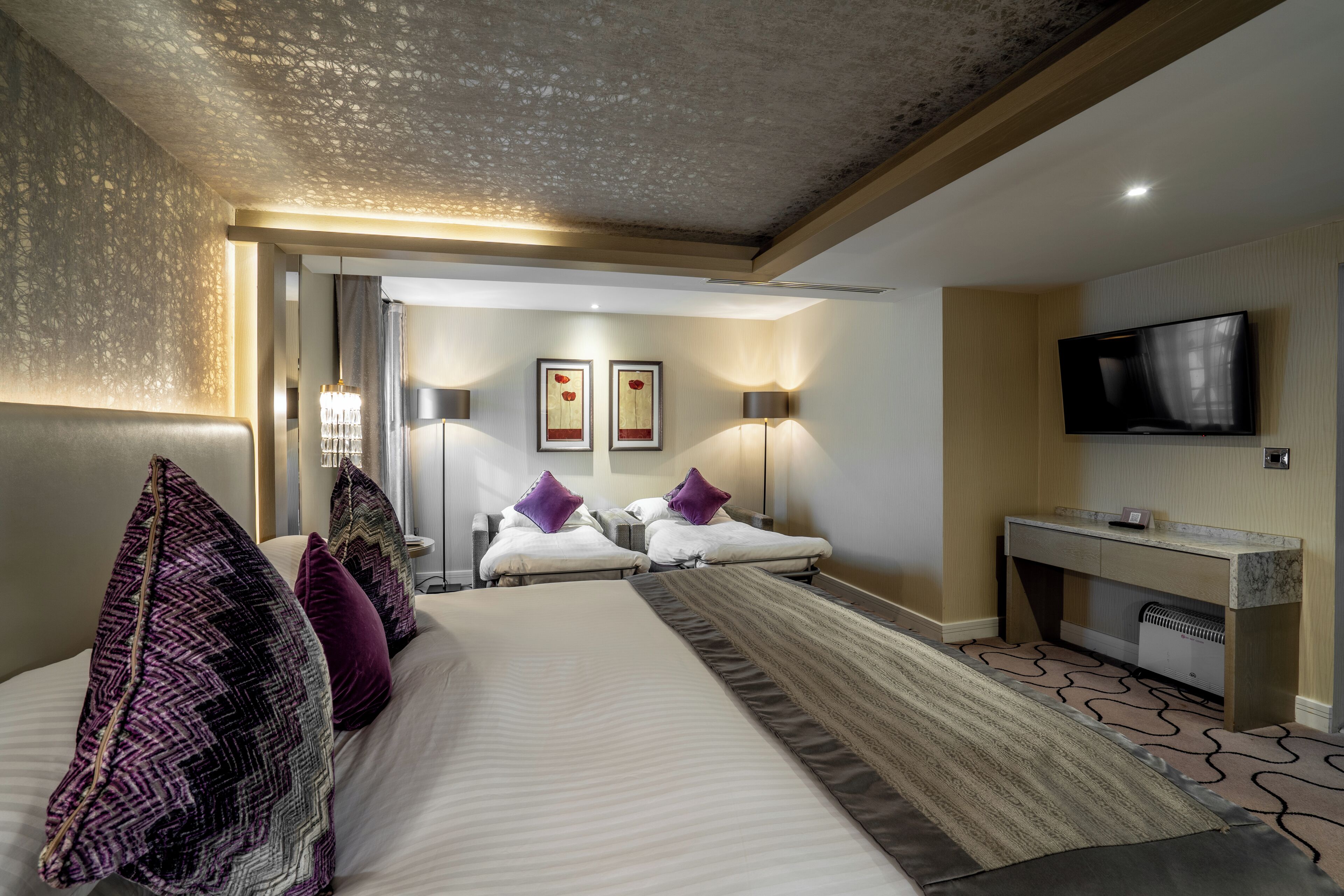 Ein Hotelzimmer mit einem großen Bett, einem Schreibtisch, einem Flachbildfernseher und zwei Wandleuchten.