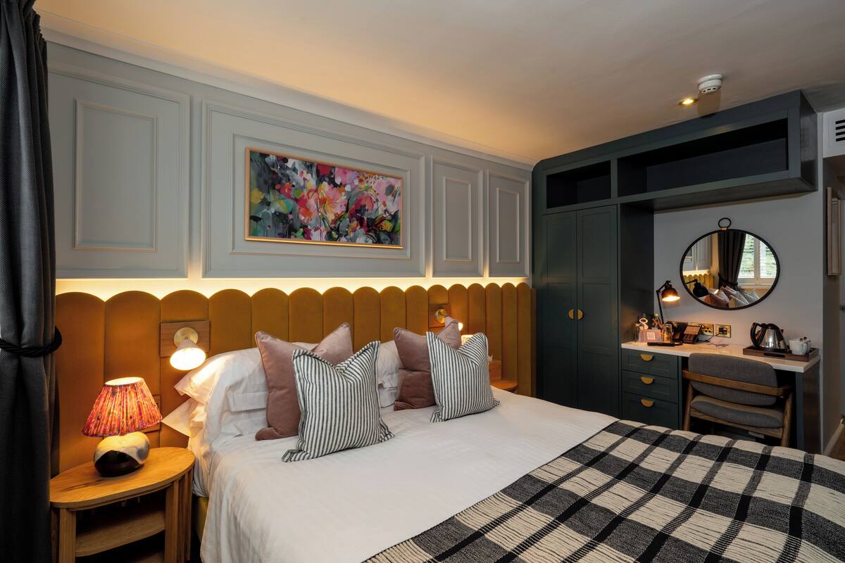 A well-lit bedroom with a bed, bedside table, lamp, and a desk with a chair.
