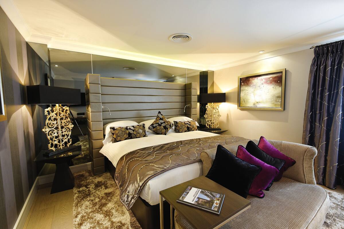 A modern hotel room with a large bed, a sofa, a small table, and a flat-screen TV.