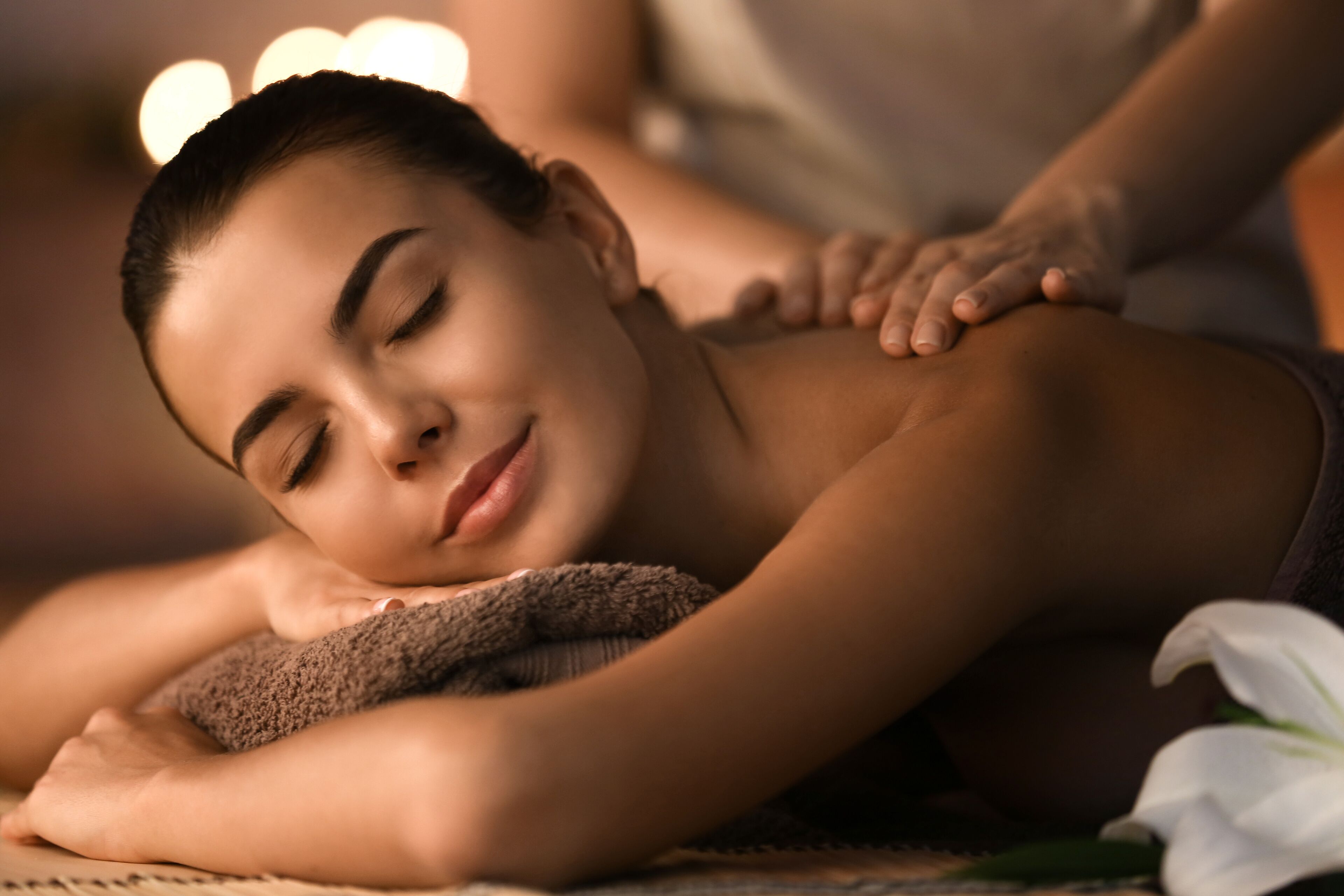 A person receiving a massage with a towel and a white flower on the table.