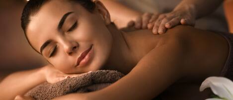 A person receiving a massage with a towel and a white flower on the table.