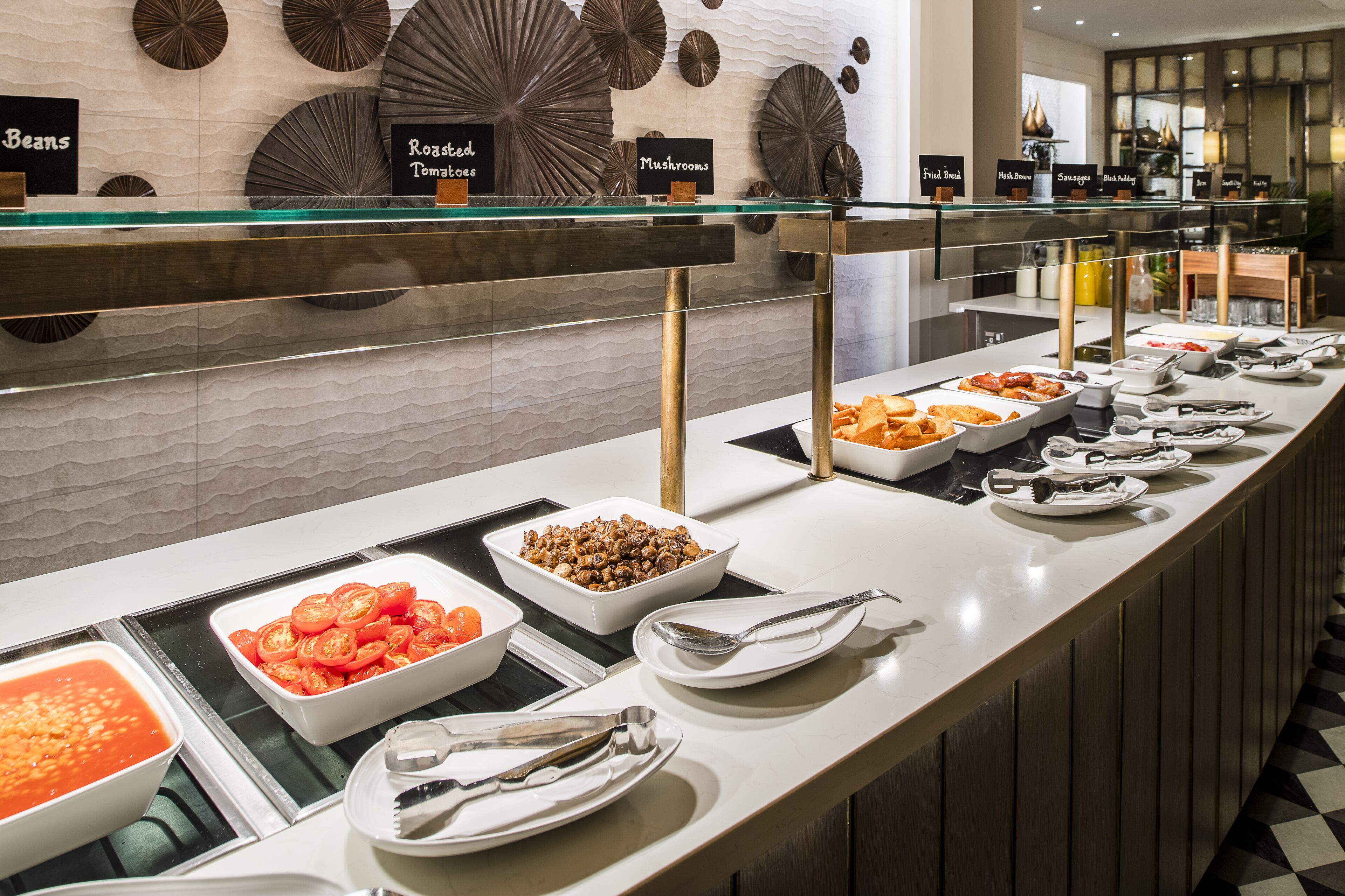 A buffet with various food options like beans, roasted tomatoes, and mushrooms.