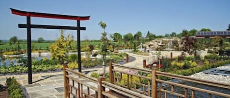 A wooden deck with a red canopy, a stone pathway, and a pond.