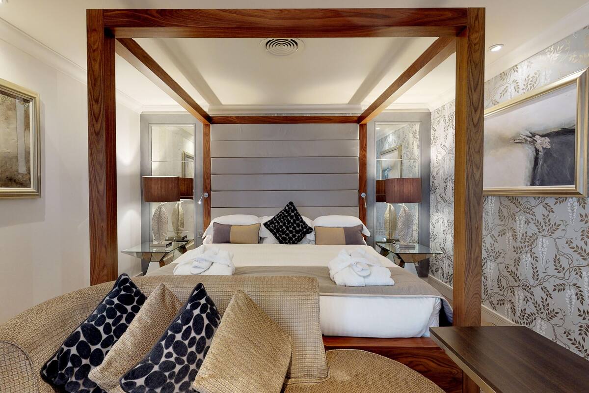 A modern hotel room with a large bed, a sofa, a small table, and a mirror.