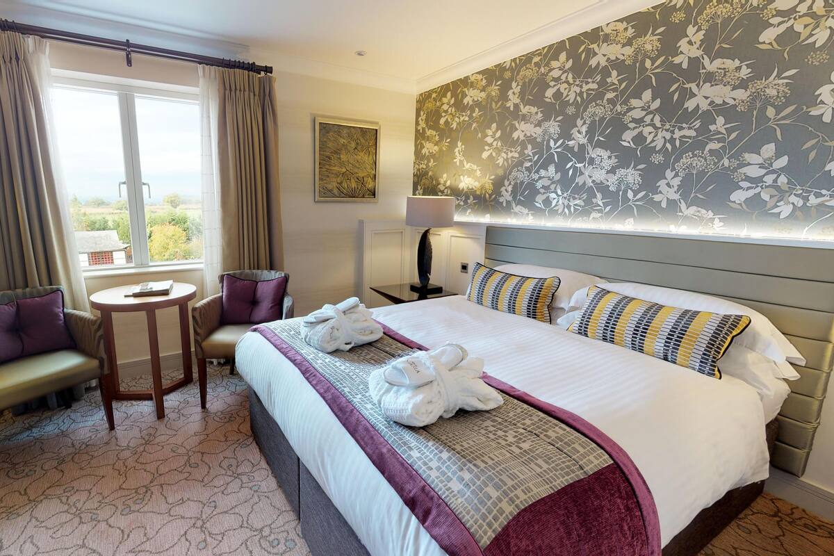A hotel room with a bed, two armchairs, a small table, a lamp, and a view of the outdoors.