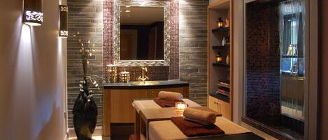 A modern spa room with a large mirror, a massage table, and a small sink.