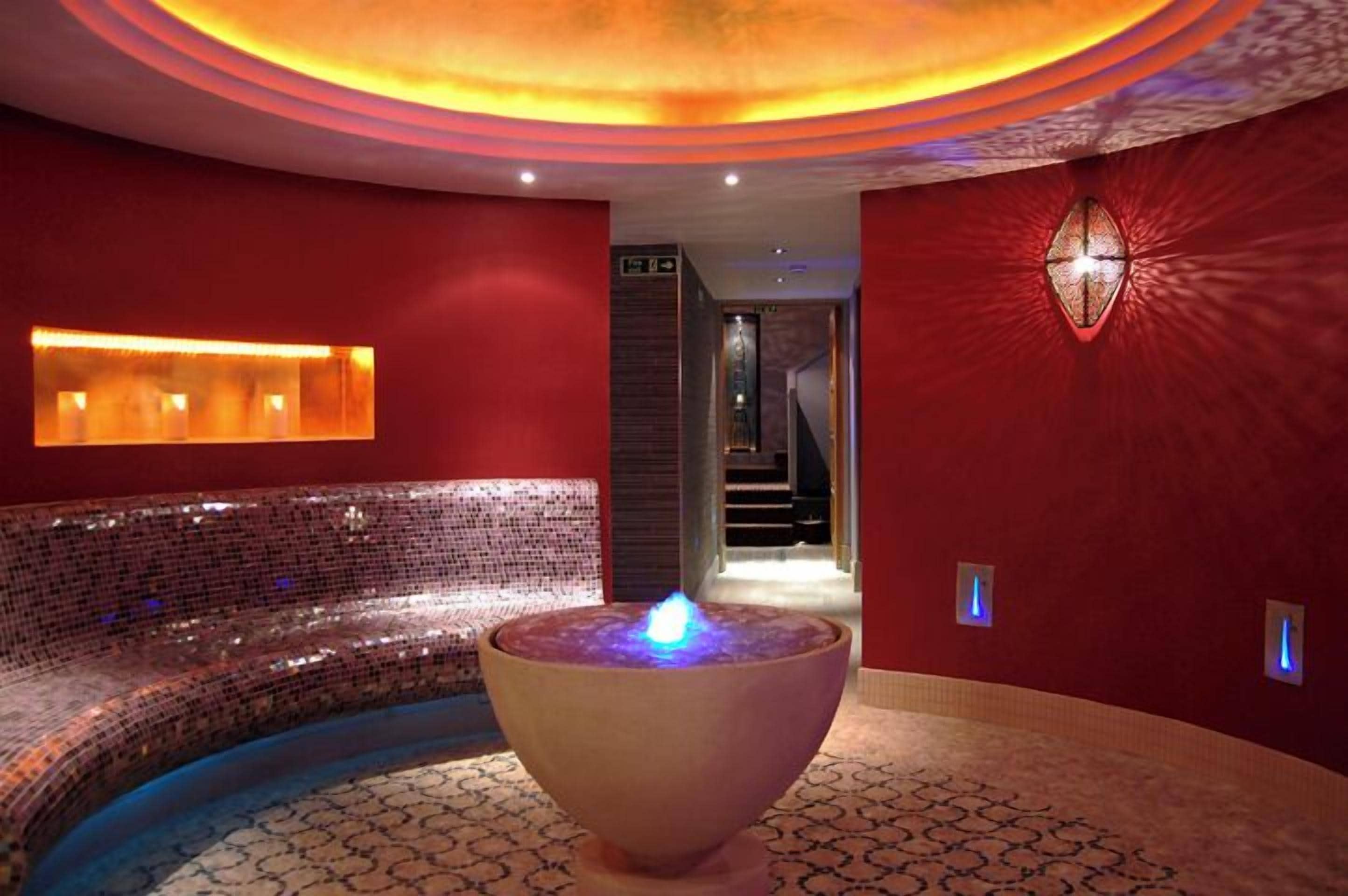 Uma área de spa com uma banheira de pedra aquecida, um acessório de iluminação fixado na parede e um piso estampado.