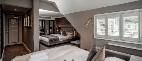 A modern hotel room with two beds, a large window with blinds, a desk, and a mirror.