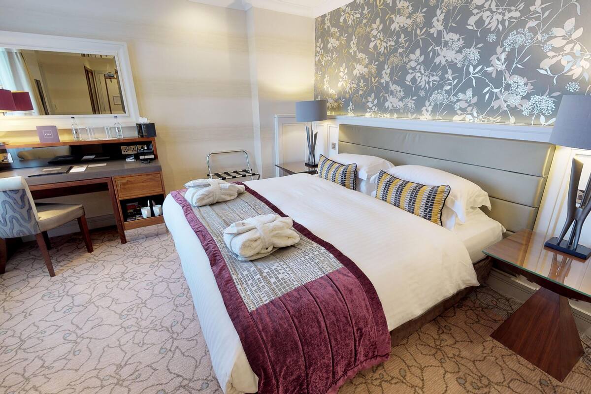 A hotel room with a bed, desk, chair, and a mirror.
