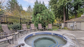 A hot tub surrounded by wicker chairs, with a metal fence and tall trees in the background.
