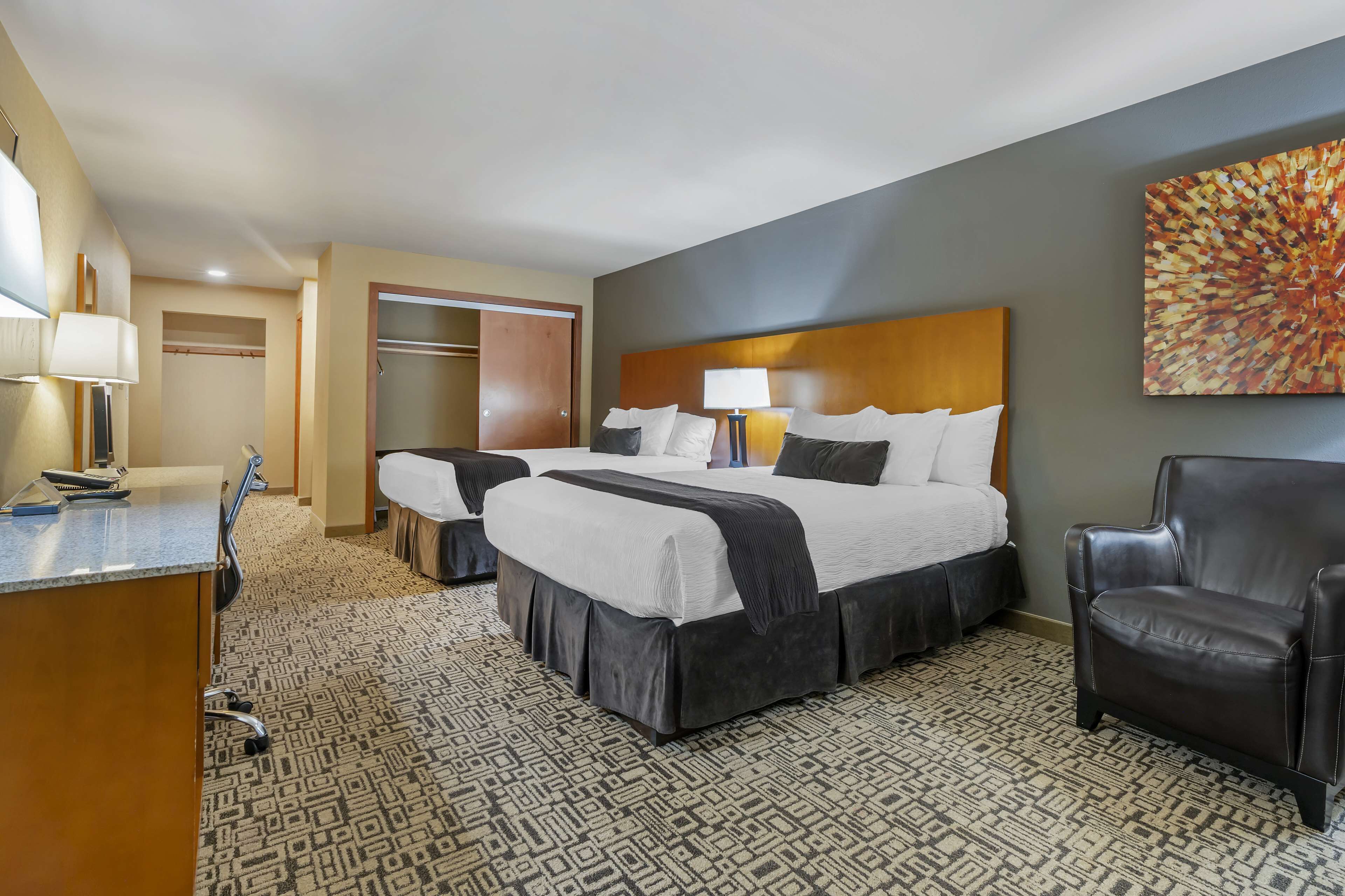 A hotel room with a large bed, two bedside tables, a desk, a chair, and a painting on the wall.
