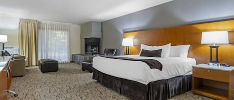 Habitación de hotel con una cama grande, dos mesitas de noche con lámparas, un escritorio con silla, un sofá, un televisor y una chimenea.