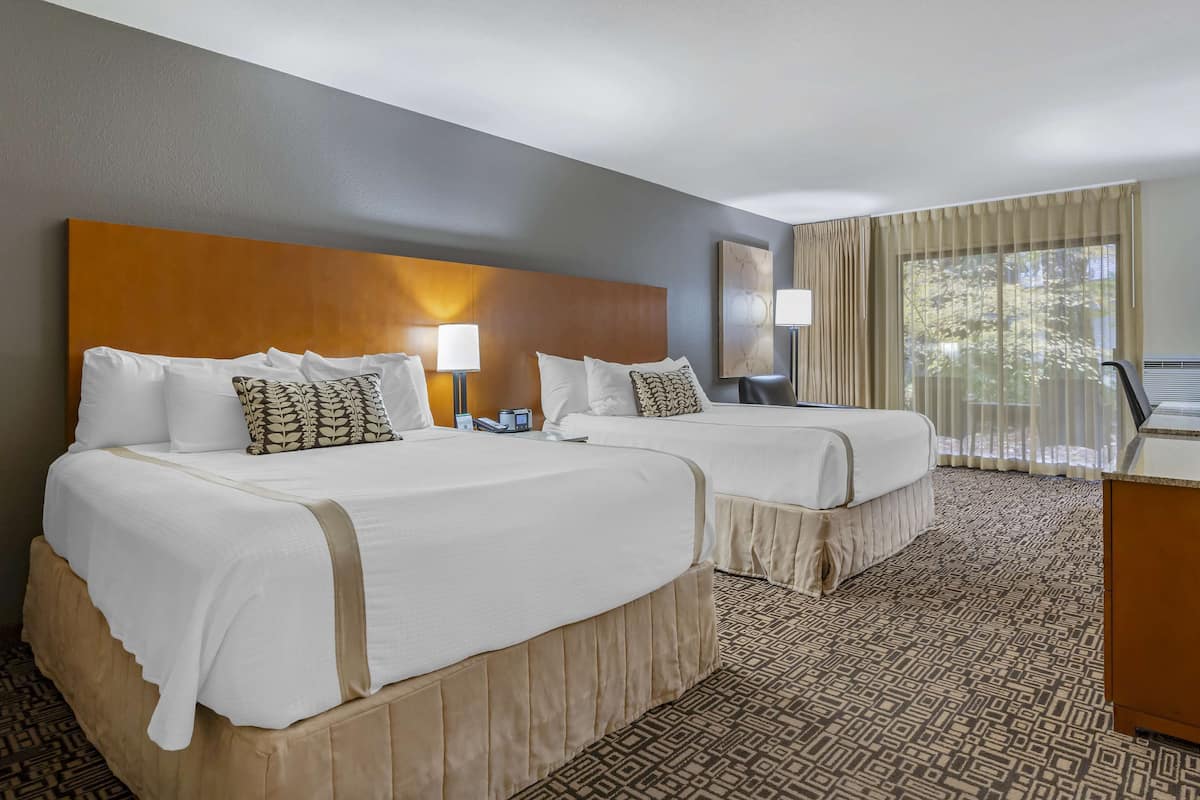 A hotel room with two beds, a large window with curtains, a desk, and a patterned carpet.