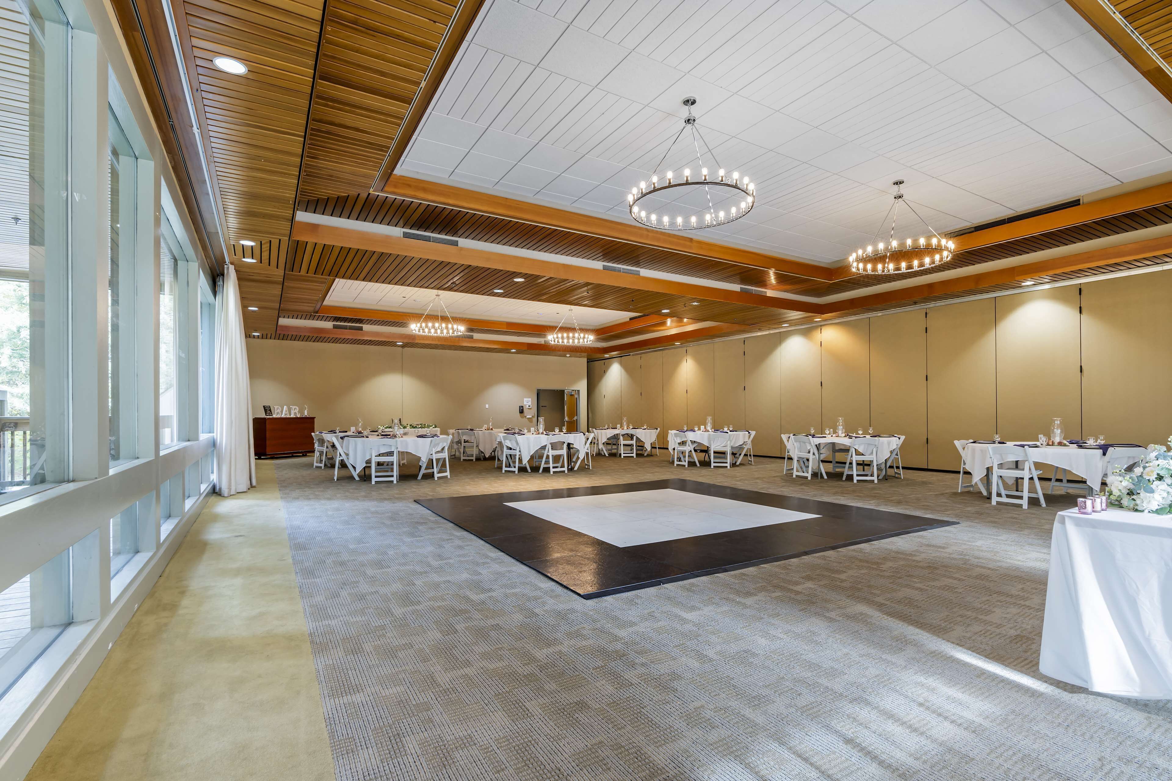 A spacious banquet hall with multiple tables set for dining, large windows on one side, and a central dance floor.
