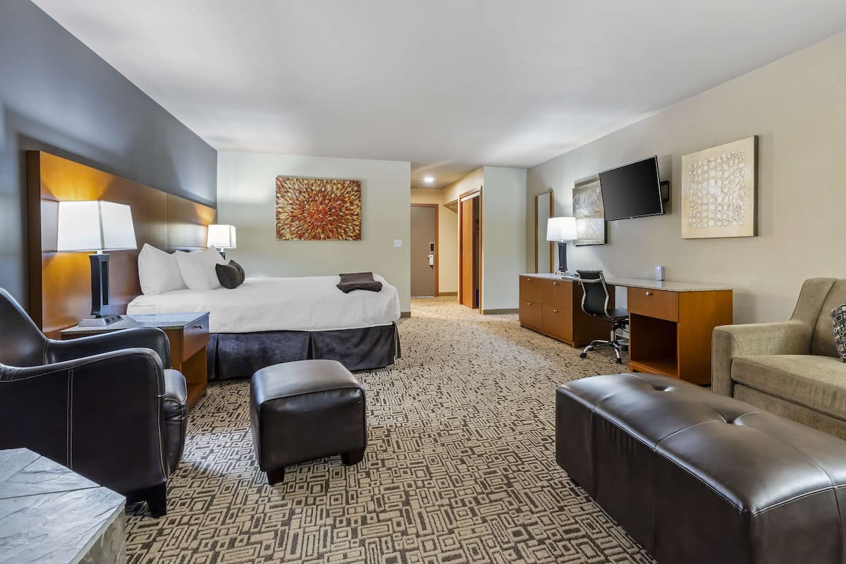 A hotel room with a bed, two chairs, a desk, a television, and artwork on the walls.