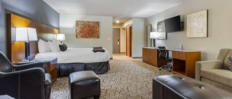 A hotel room with a bed, two chairs, a desk, a television, and artwork on the walls.