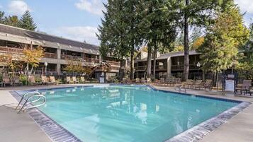 A rectangular swimming pool with a tiled edge, surrounded by lounge chairs and a covered seating area with a railing.