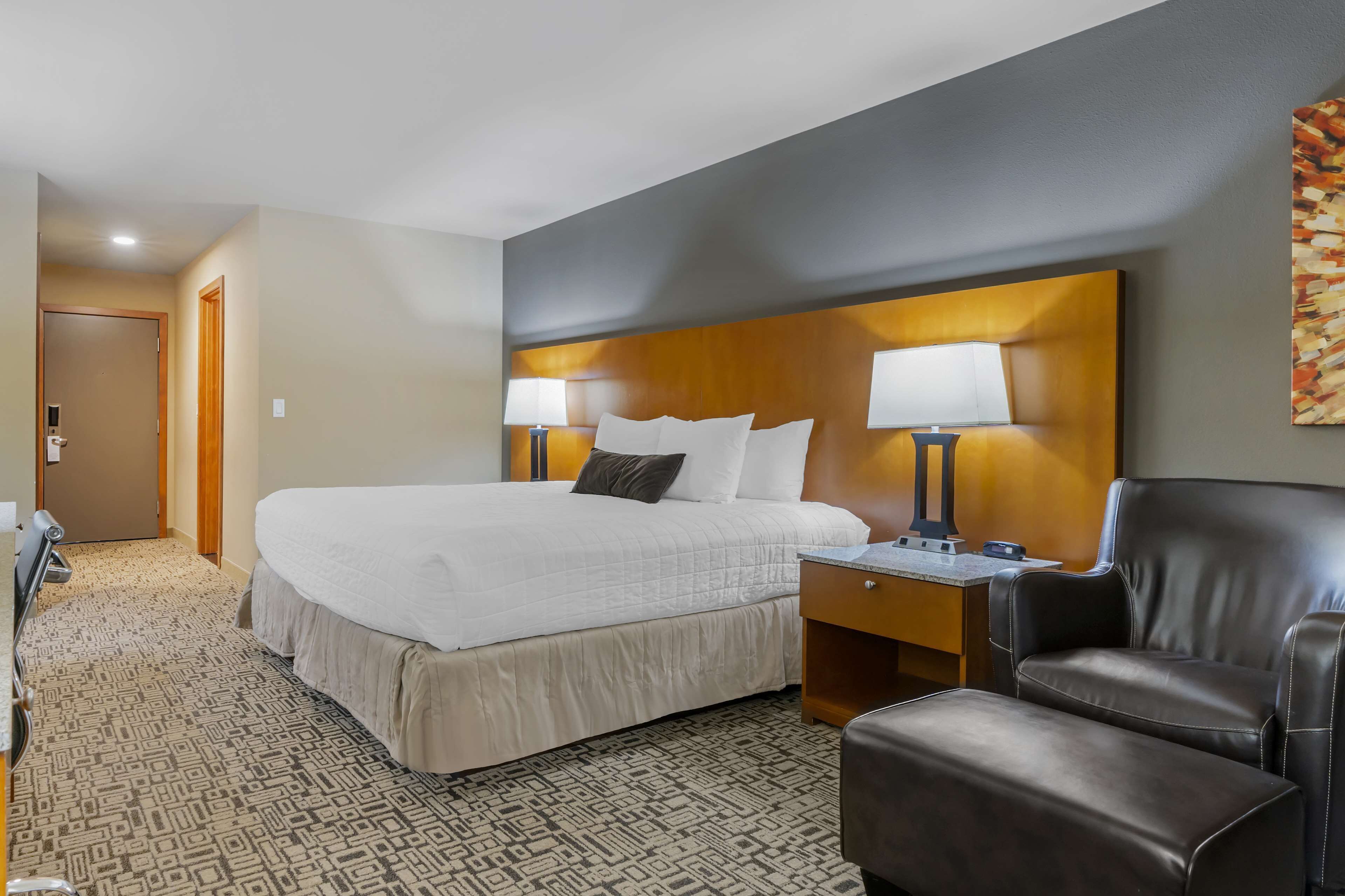 Een hotelkamer met een groot bed, twee bedlampen, een leren fauteuil en een kamerbreed tapijt met een patroon.