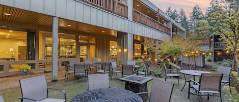 An outdoor patio with tables and chairs, a covered seating area, and a view of the surrounding trees and sky.