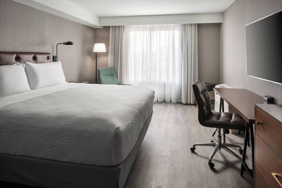 Une chambre d’hôtel avec un grand lit, un bureau, une chaise, une télévision et une fenêtre avec des rideaux.
