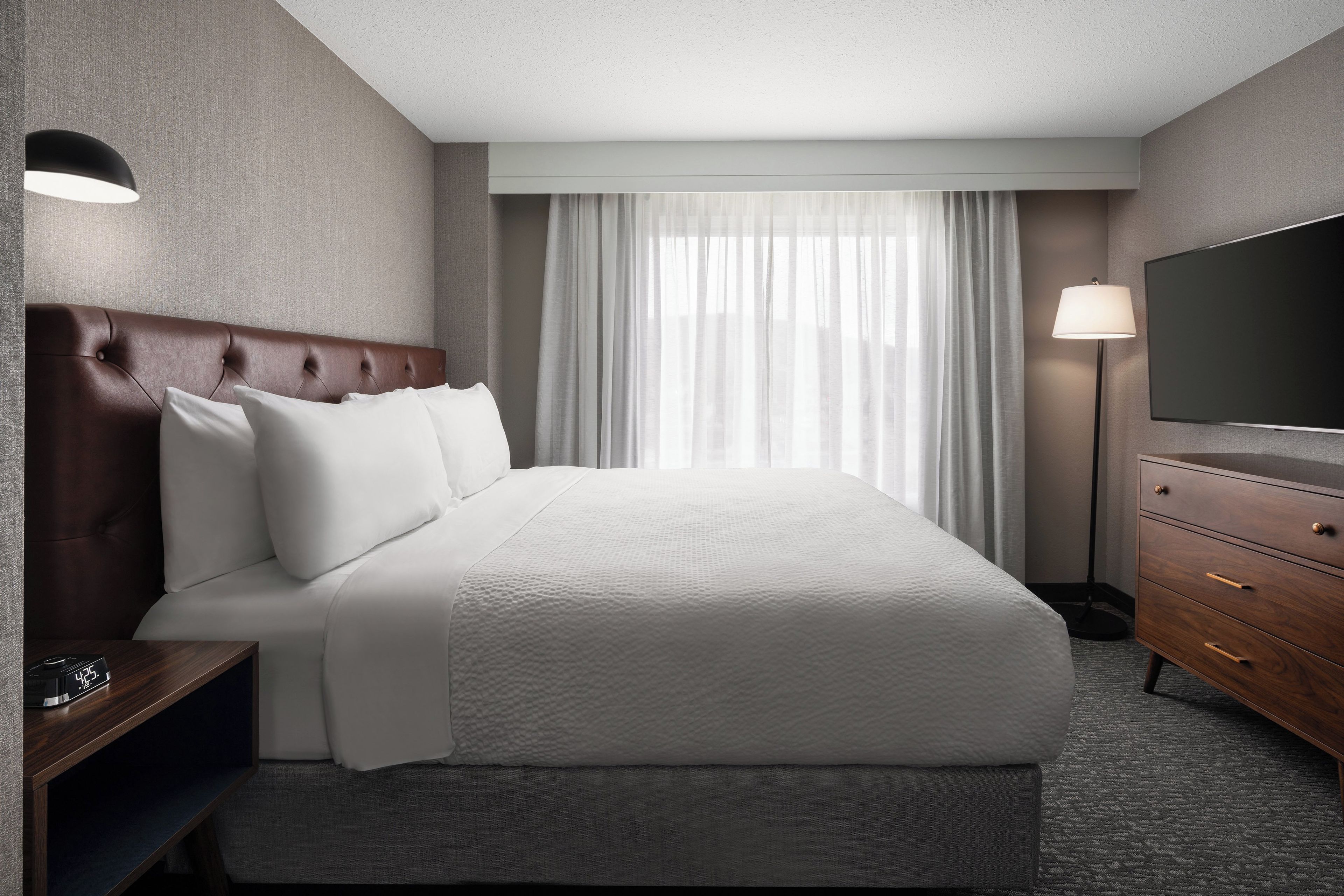 Habitación de hotel con una cama grande, un televisor de pantalla plana, una mesita de noche y una lámpara.