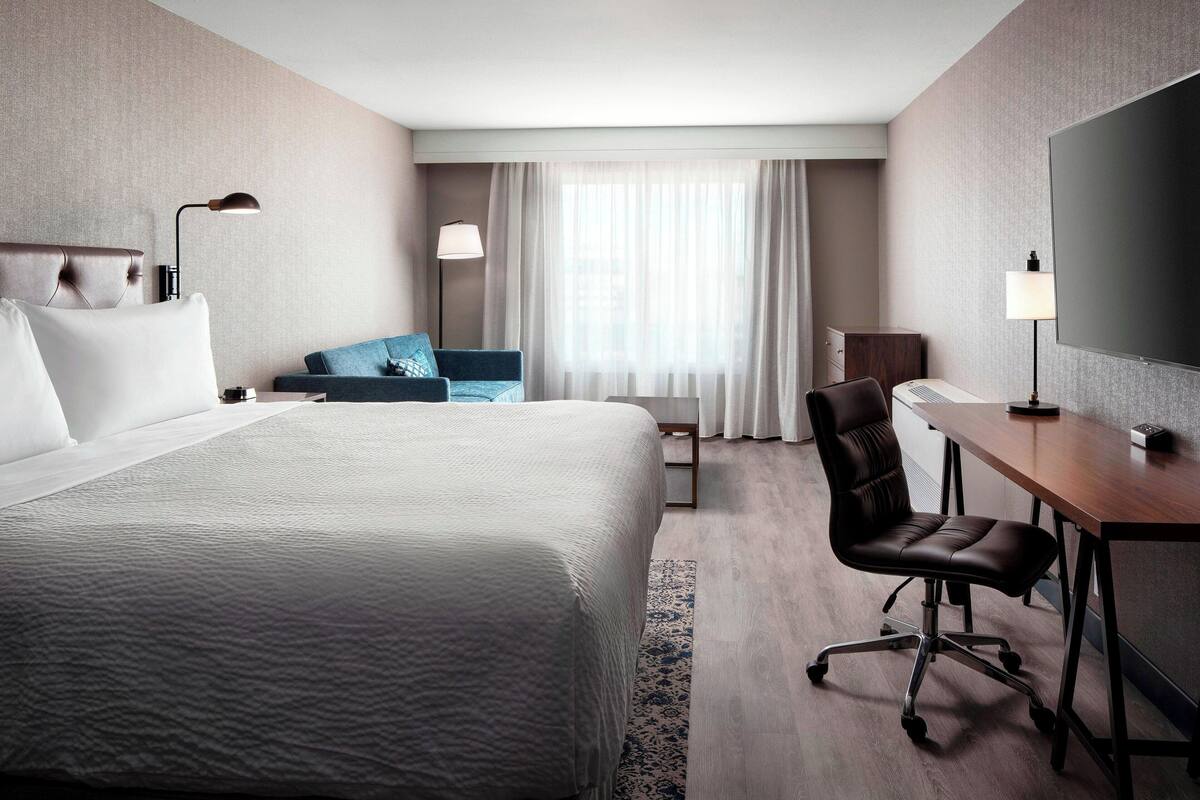 Une chambre d’hôtel avec un grand lit, un bureau, une chaise, une télévision et une fenêtre avec des rideaux.