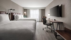Una habitación de hotel con dos camas, un escritorio, una silla, un televisor y una ventana con cortinas.