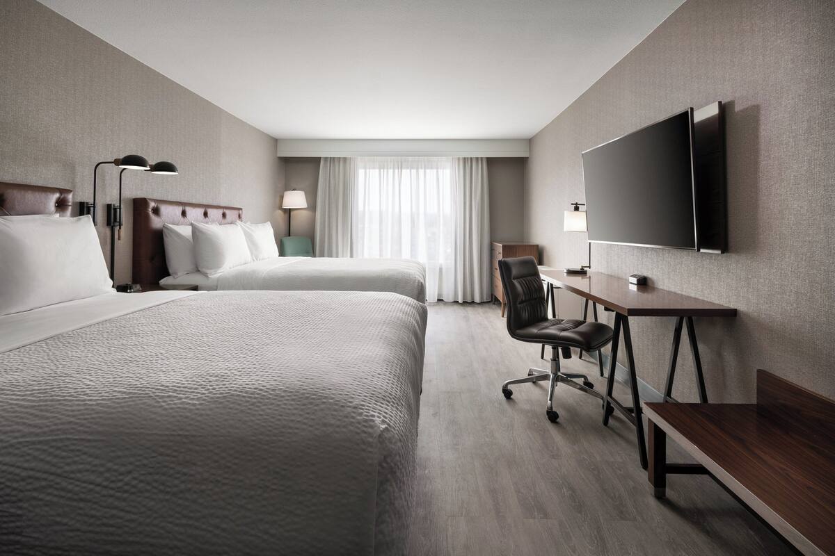 Une chambre d’hôtel avec deux lits, un bureau, une chaise, une télévision et une fenêtre avec des rideaux.