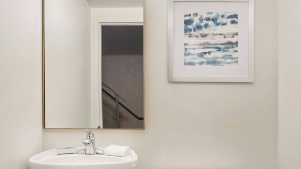 A bathroom with a pedestal sink, a toilet, a framed abstract painting, and a mirror with a gold frame. - Four Points by Sheraton Hotel & Suites San Francisco Airport (South San Francisco)