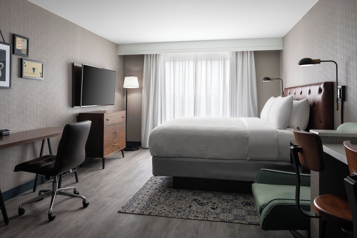 Une chambre d’hôtel équipée d’un lit, d’un bureau, d’une chaise, d’une télévision et de rideaux.