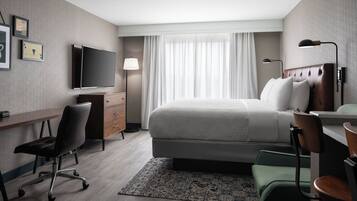 Una habitación de hotel con cama, escritorio, silla, televisor y cortinas.
