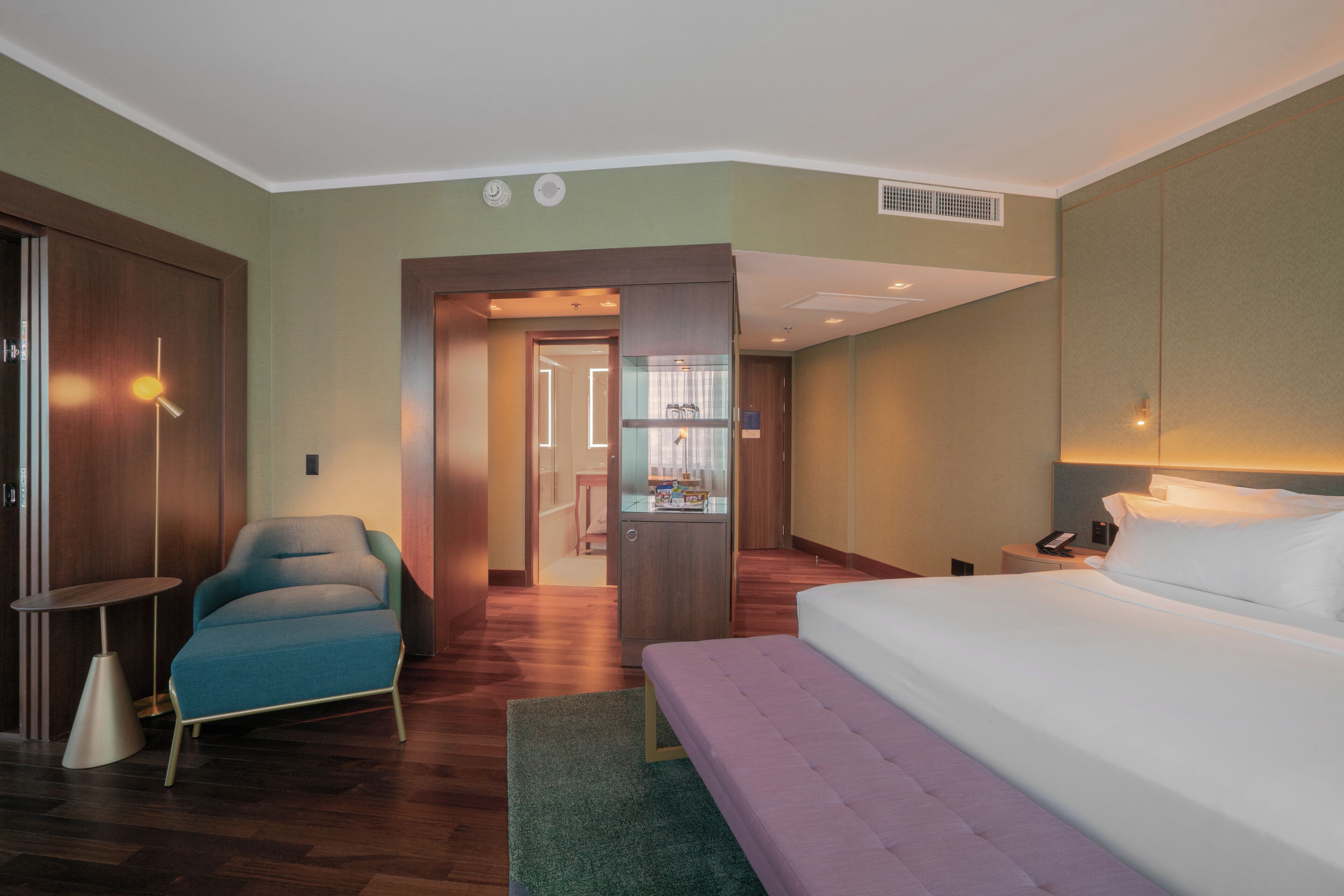 A hotel room with a bed, a chair, a desk, and a wardrobe.