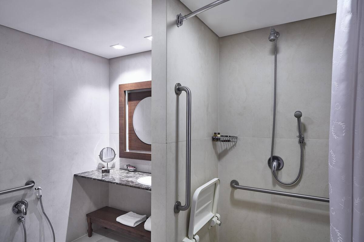 Een moderne badkamer met een douche, handgrepen, een wastafel en een spiegel.